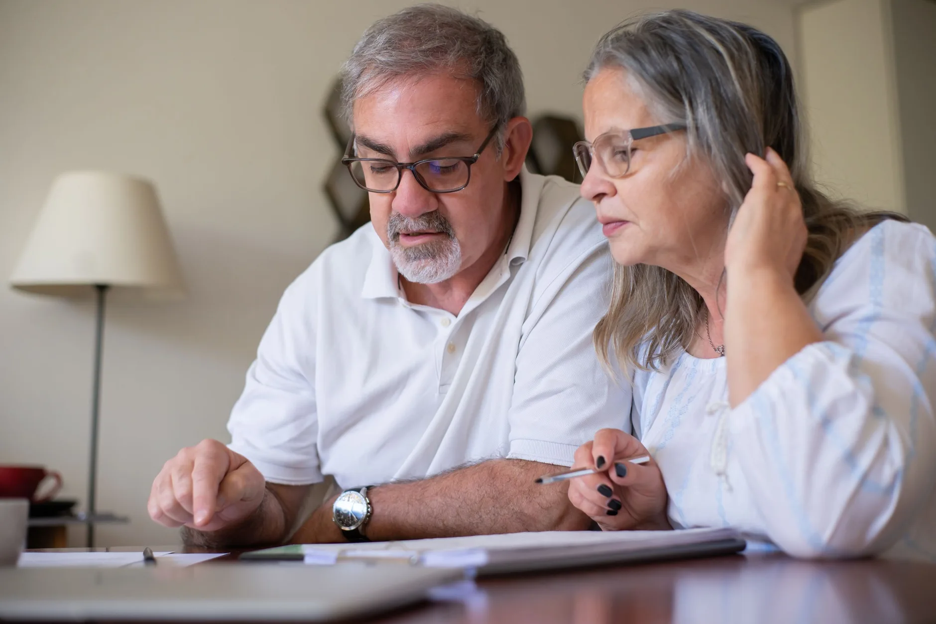 An older couple sitting together at a dining table, reading through paperwork with a pencil in hand