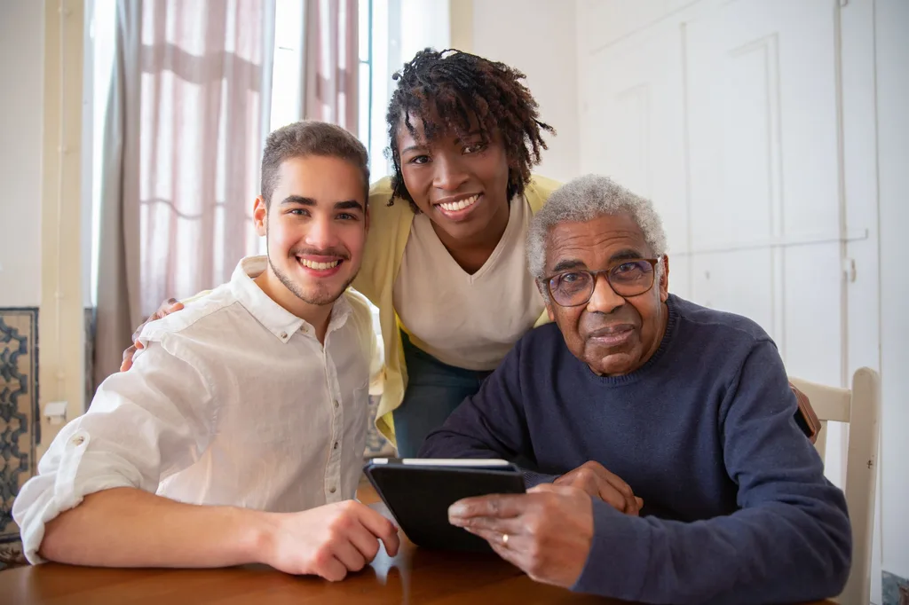 An older man reviewing a plan on a tablet with two younger family members at the kitchen table