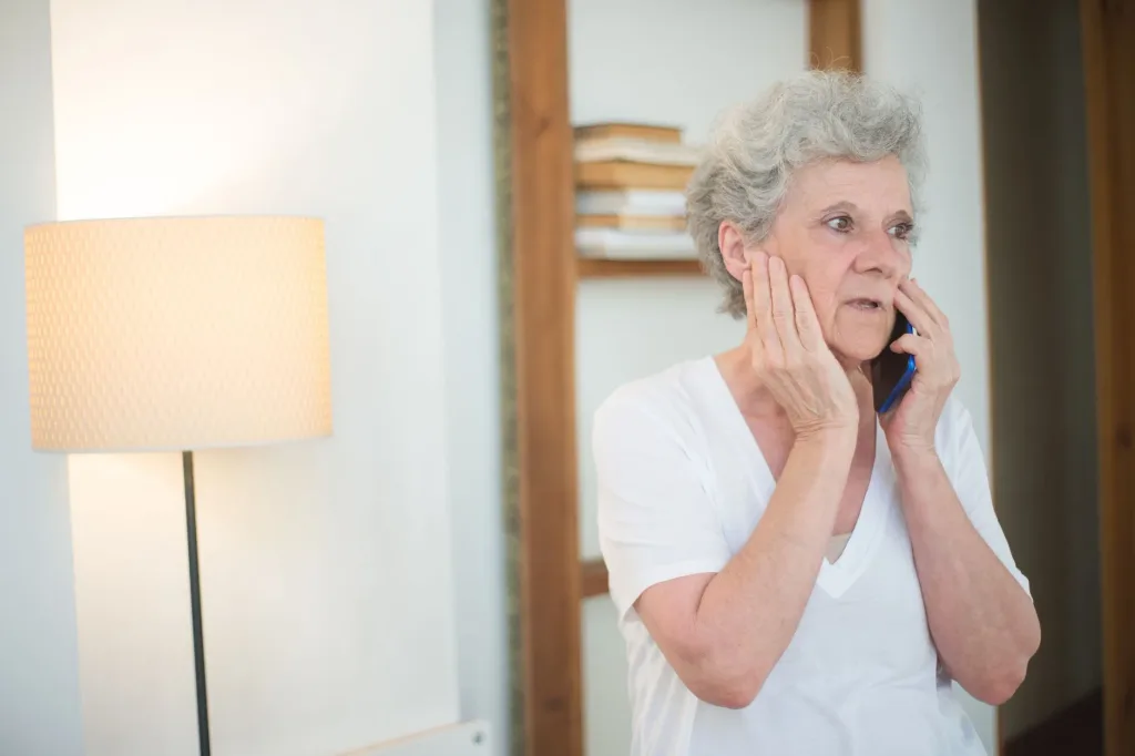 An older woman with grey hair holding a mobile phone to her ear, looking wary