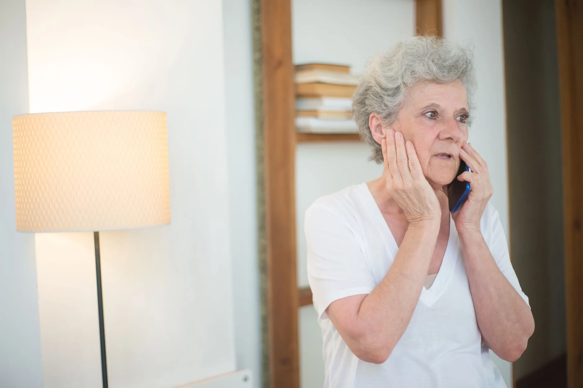 An older woman with grey hair holding a mobile phone to her ear, looking wary