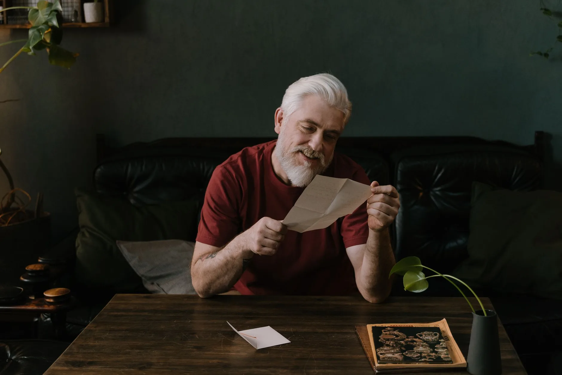 An older man with white hair reading a letter at a wooden table at home
